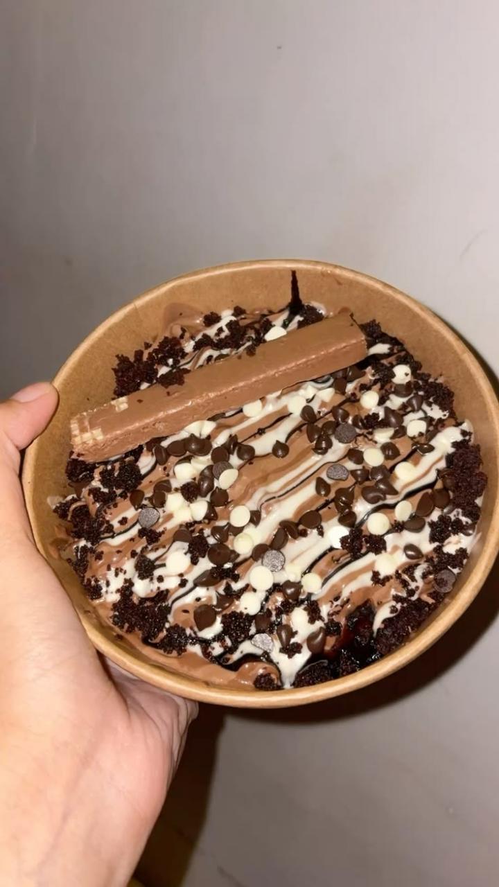A round dessert tub topped with chocolate drizzle, sprinkles and chocolate pieces